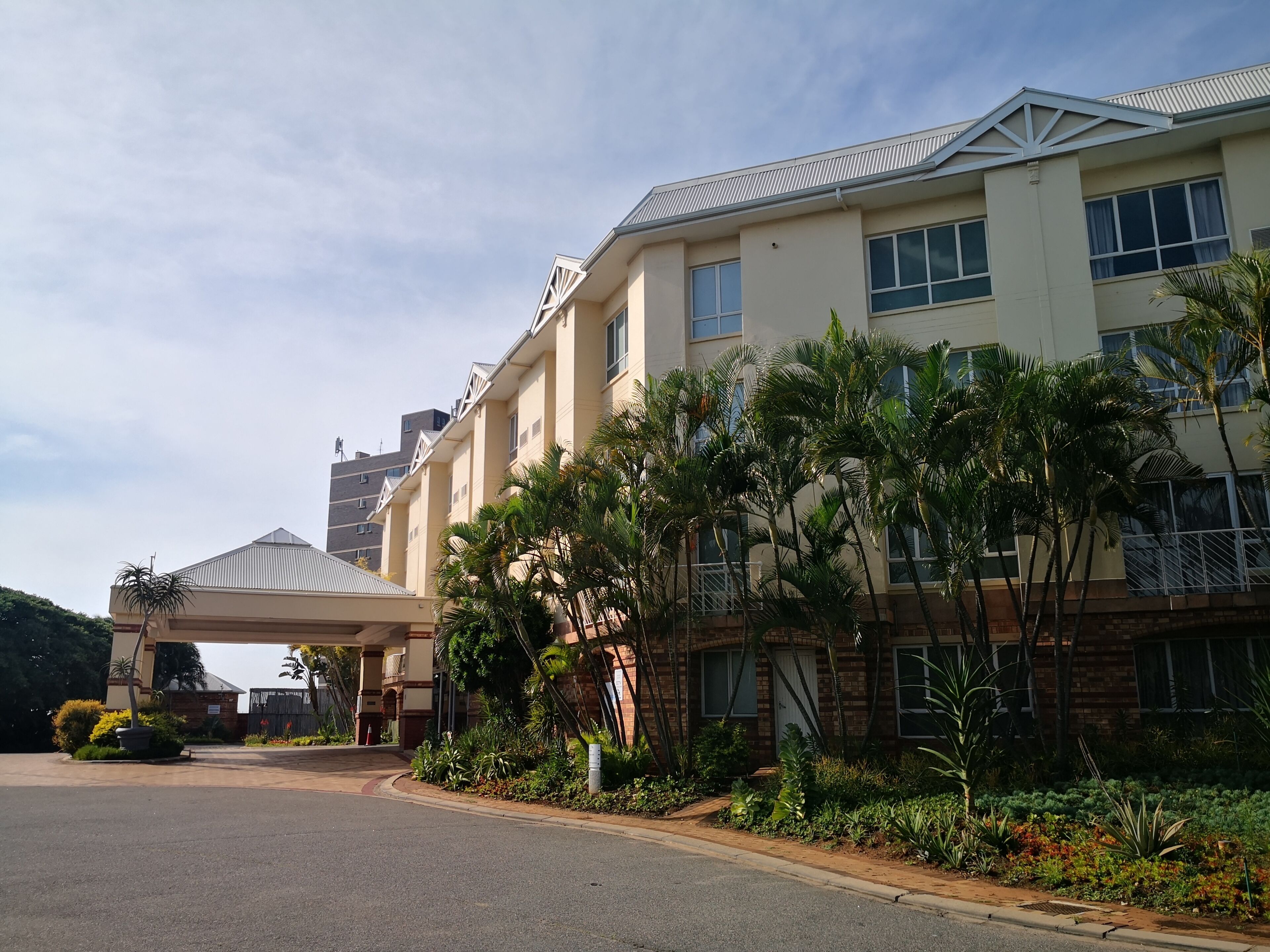 Een meerlaags hotel met een overdekte ingang, palmbomen en een gevel van baksteen.