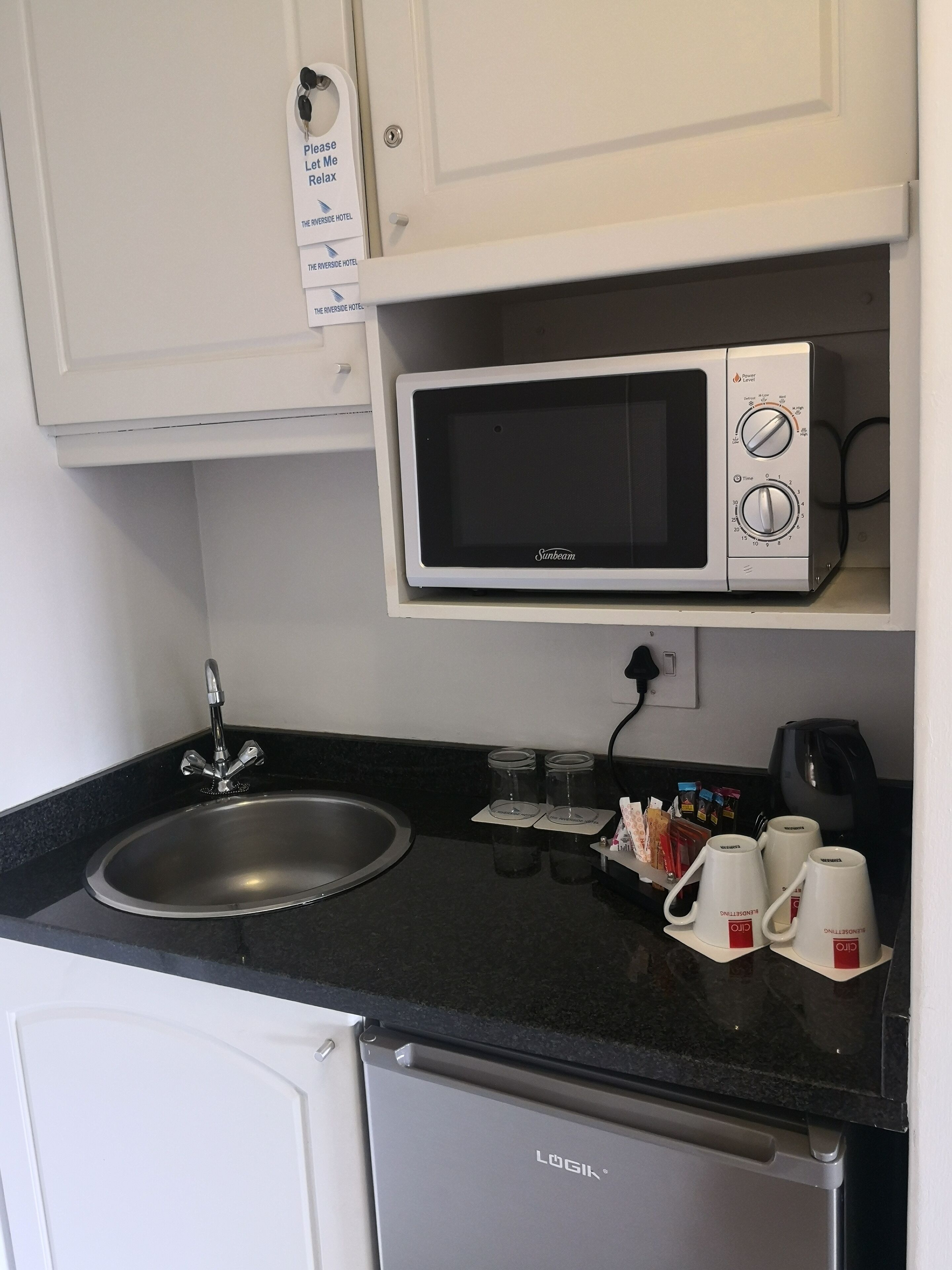 Una kitchenette compacta con microondas, lavamanos y cafetera.