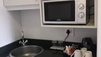 Una kitchenette compacta con microondas, lavamanos y cafetera.