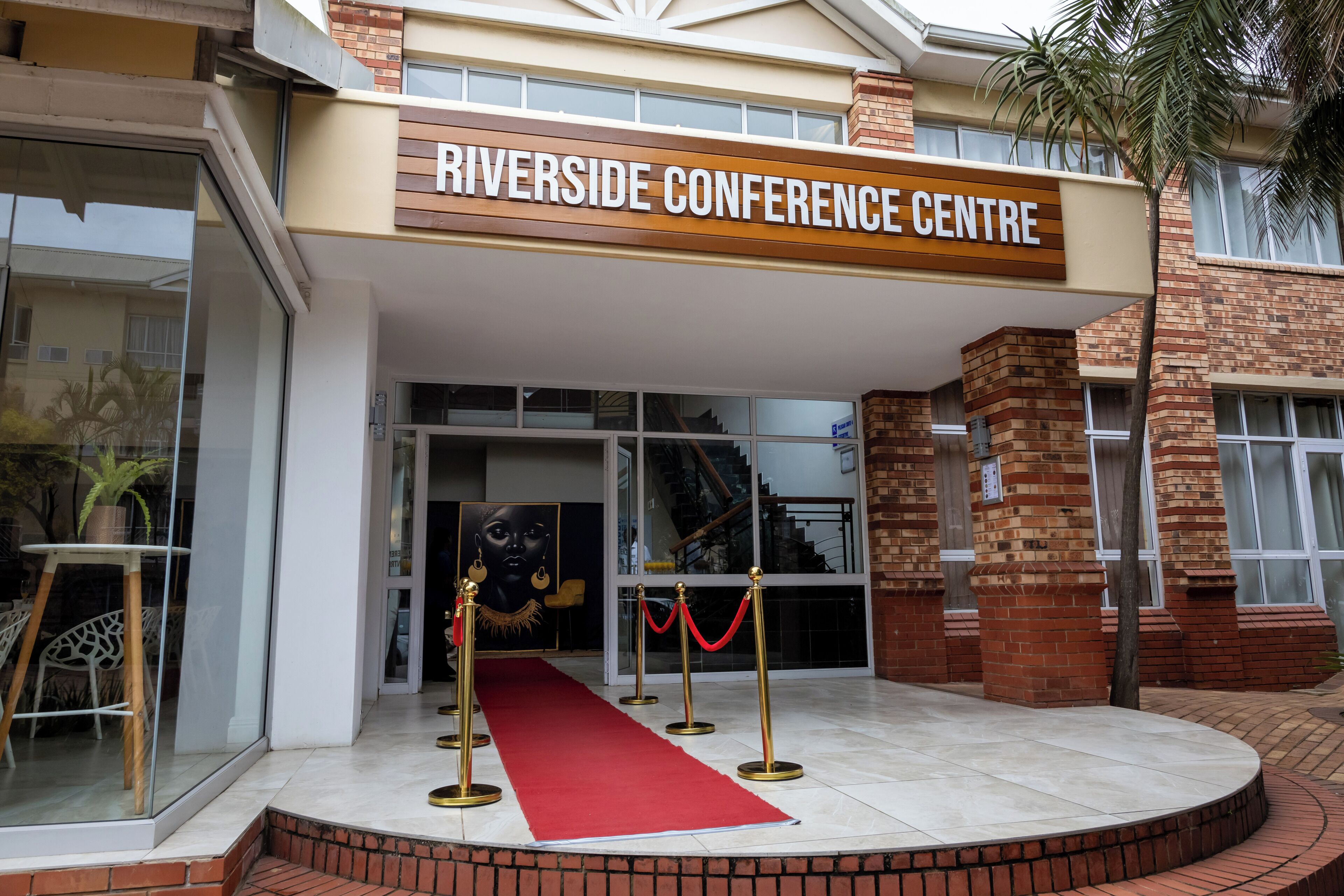 Entrada do Centro de Convenções Riverside, com tapete vermelho, portas de vidro e escadaria para o interior.