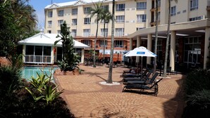 A hotel courtyard with a swimming pool, lounge chairs, and palm trees. - The Riverside Hotel (Durban North)