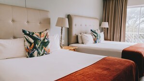 A hotel room with two beds, each with a headboard and a bedside table with a lamp. - The Riverside Hotel (Durban North)