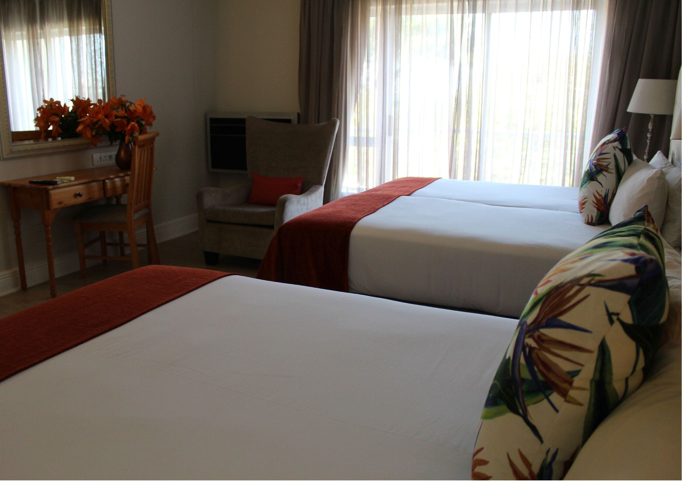 A hotel room with two beds, a desk, a chair, and a window with curtains.