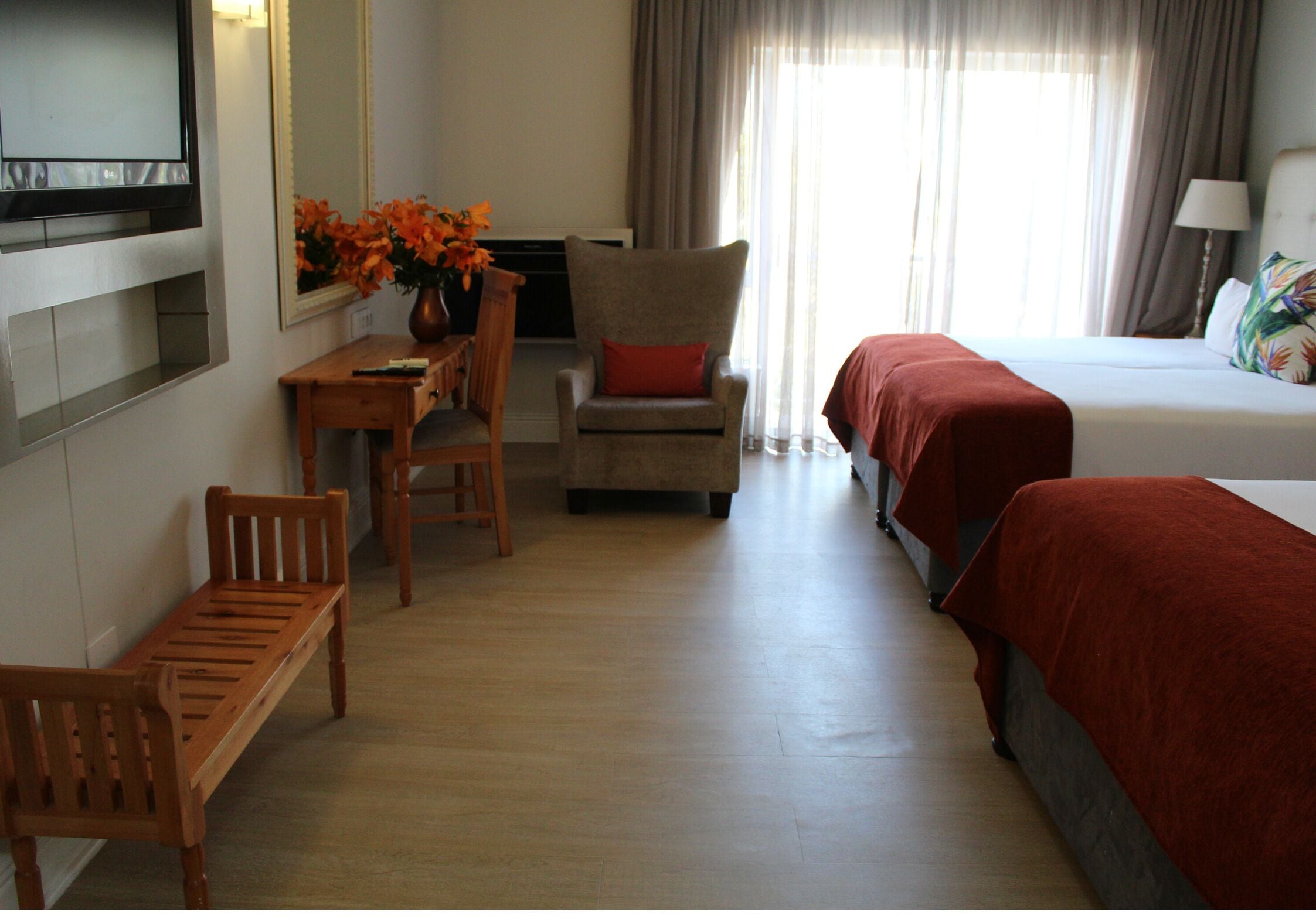 Habitación de hotel con cama, escritorio con silla, televisor y un florero con flores.
