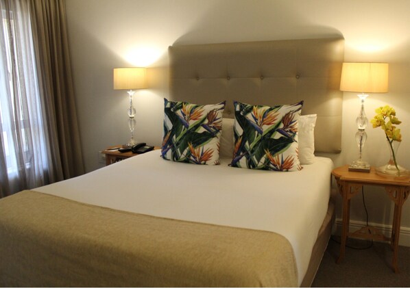 A hotel room with a large bed, two bedside lamps, a wooden nightstand, and a vase with flowers.