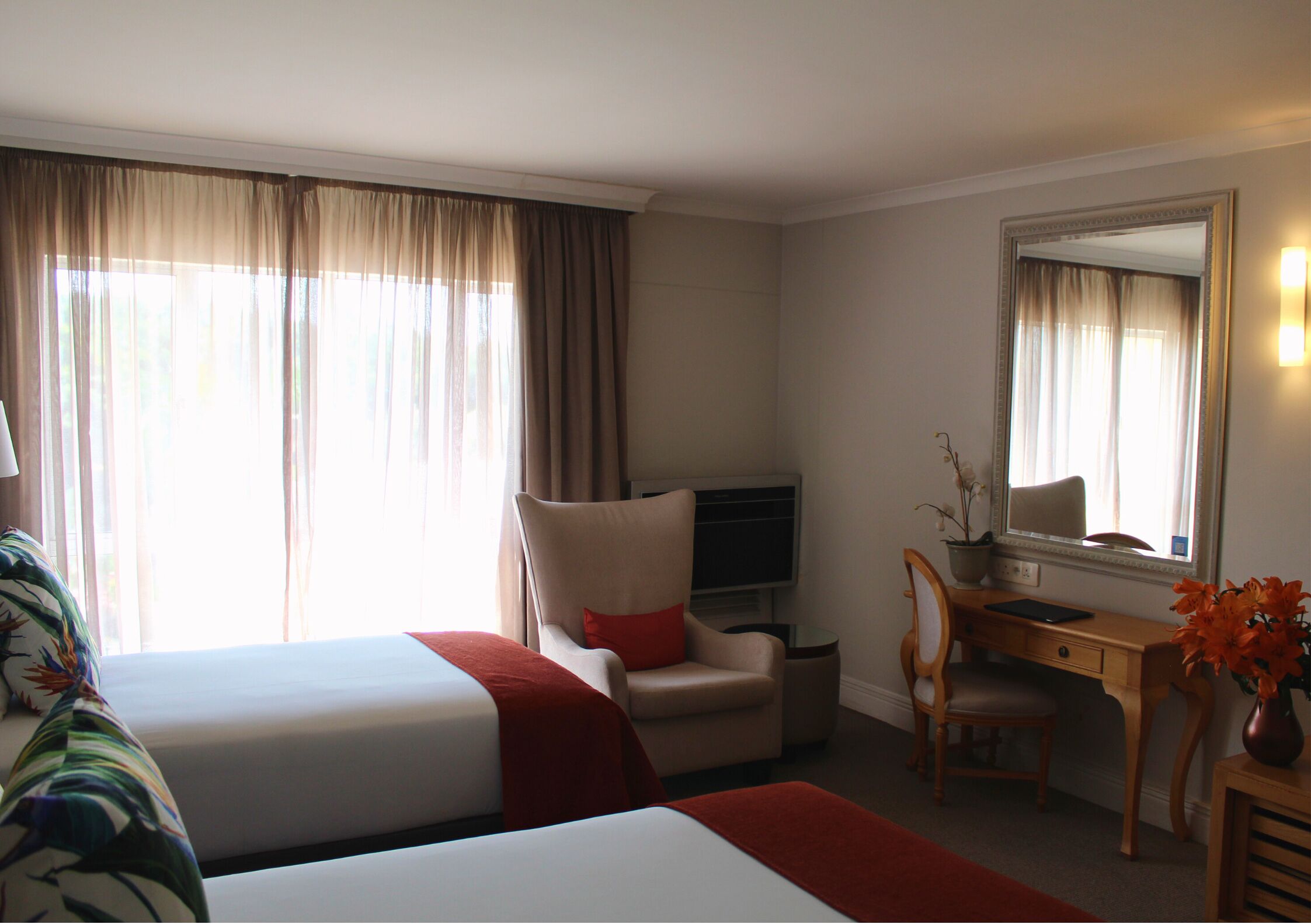 A hotel room with two beds, a desk, a chair, a TV, and a large mirror.