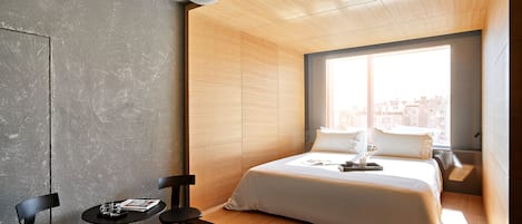 Une chambre moderne avec un lit en bois, une petite table, deux chaises et une grande fenêtre donnant sur la ville.