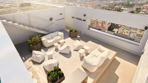 Terraza en la azotea con sofás blancos, jardineras y vistas a la ciudad.