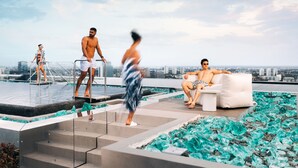 Zona de piscina en la azotea con suelo de vidrio, vistas a la ciudad y un área de descanso con un sofá blanco y una mesita.