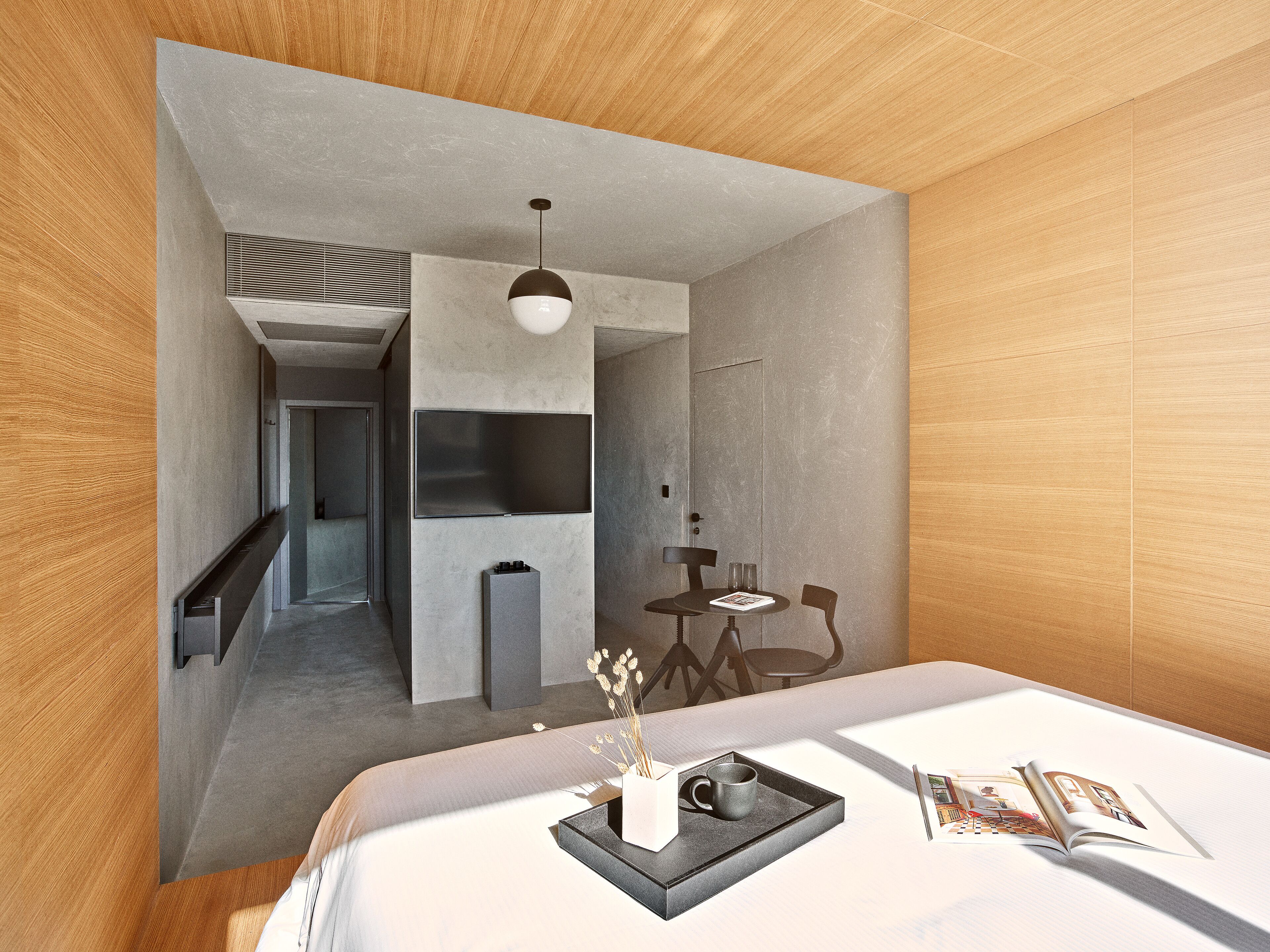 A modern hotel room with a bed, a small dining area, and a kitchenette.