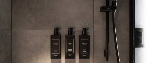 A modern bathroom with a sleek design, featuring a wall-mounted shower, a handheld showerhead, and three bottles of Culti shampoo.