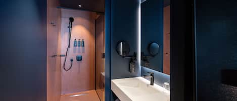 A modern bathroom with a shower, a white sink, and a large mirror.