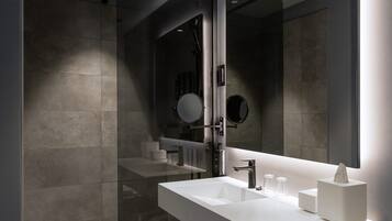 Ein modernes Badezimmer mit einer ein Glasfenster trennenden Dusche, einem großen Spiegel und einem weißen Waschtisch mit Handtuchhalter.