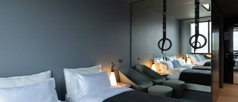 A modern hotel room with two beds, a seating area, and a large mirror reflecting the room.