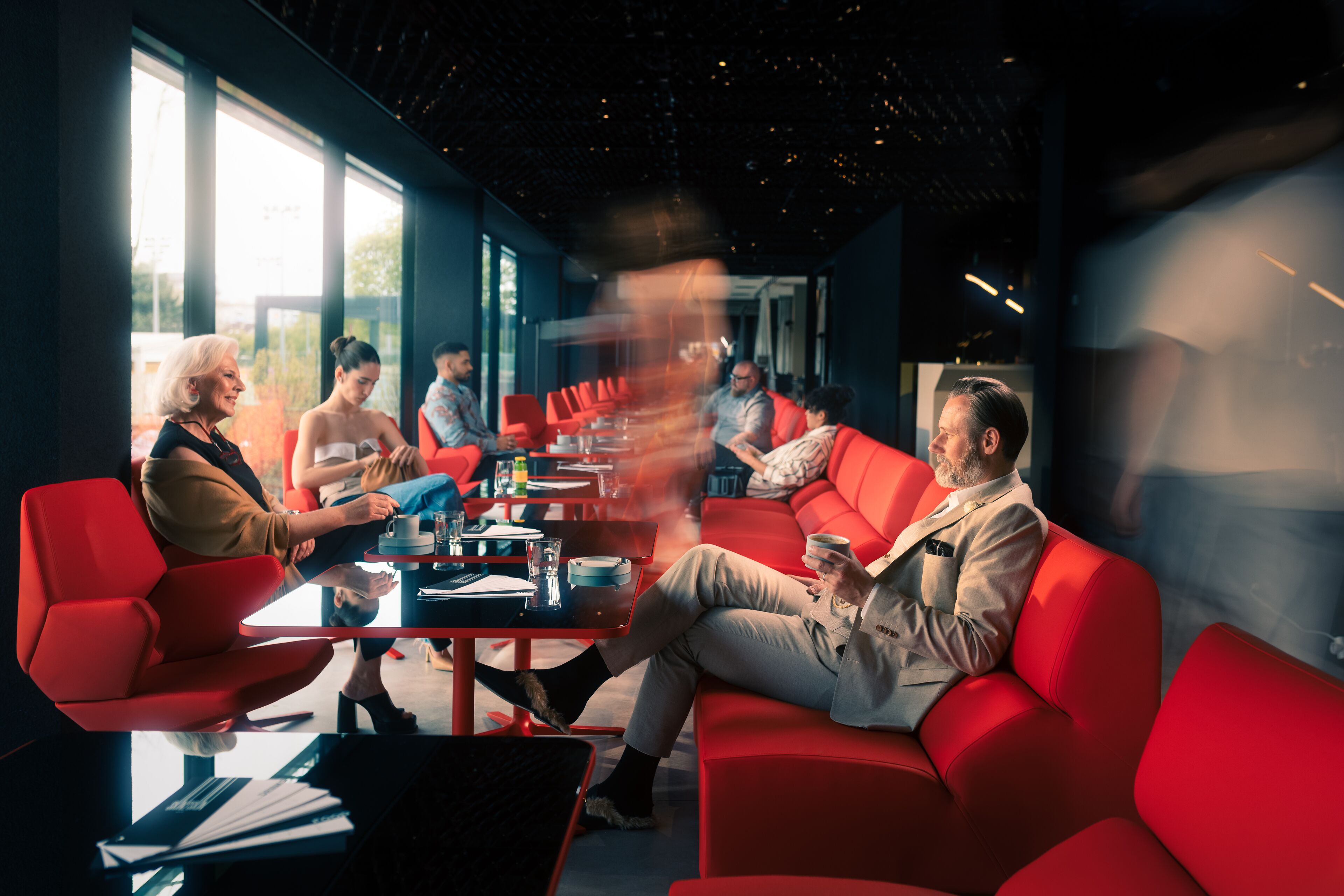 A modern meeting room with red seating, glass tables, and large windows.
