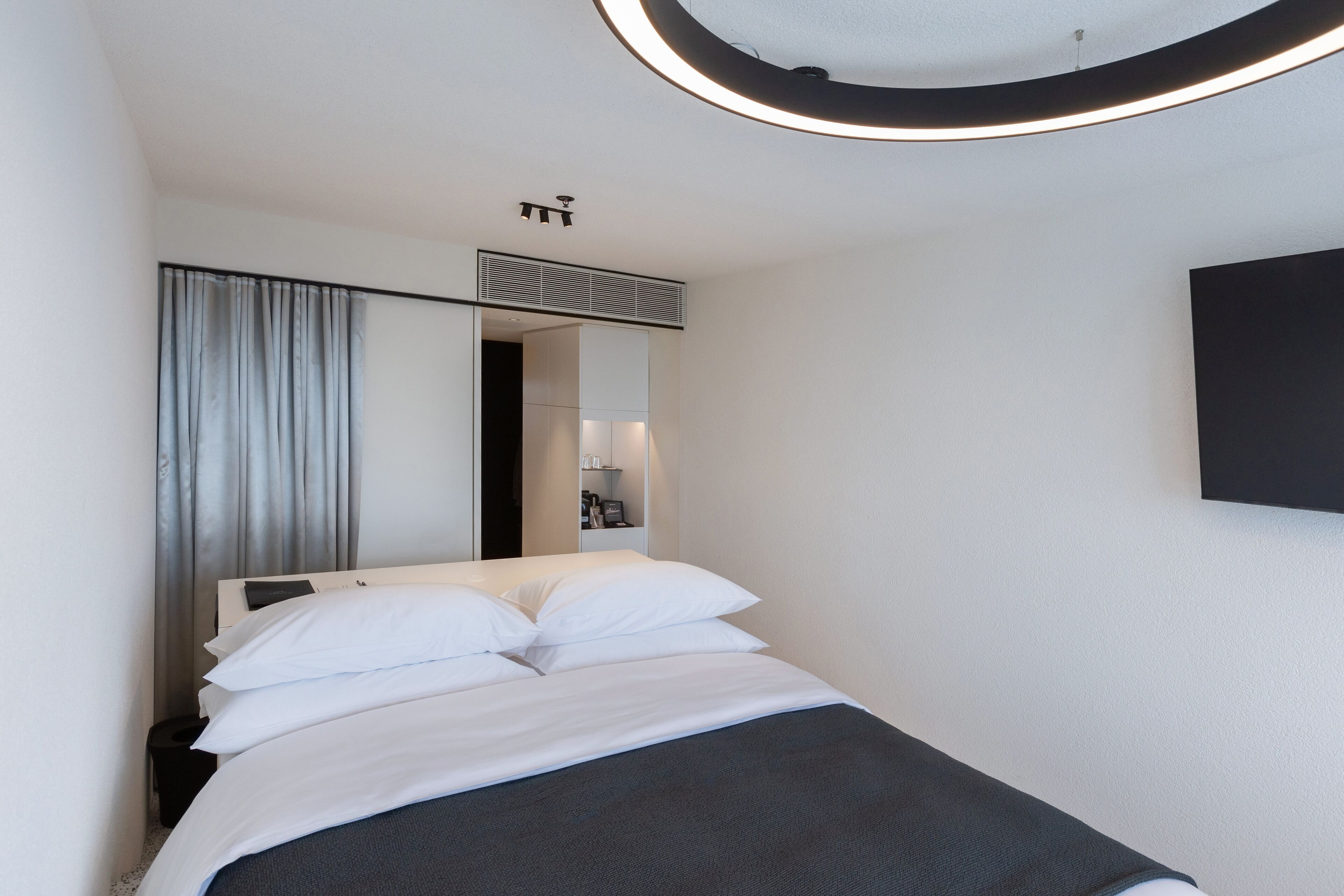 A modern hotel room with a neatly made bed, a large mirror, and a wall-mounted TV.
