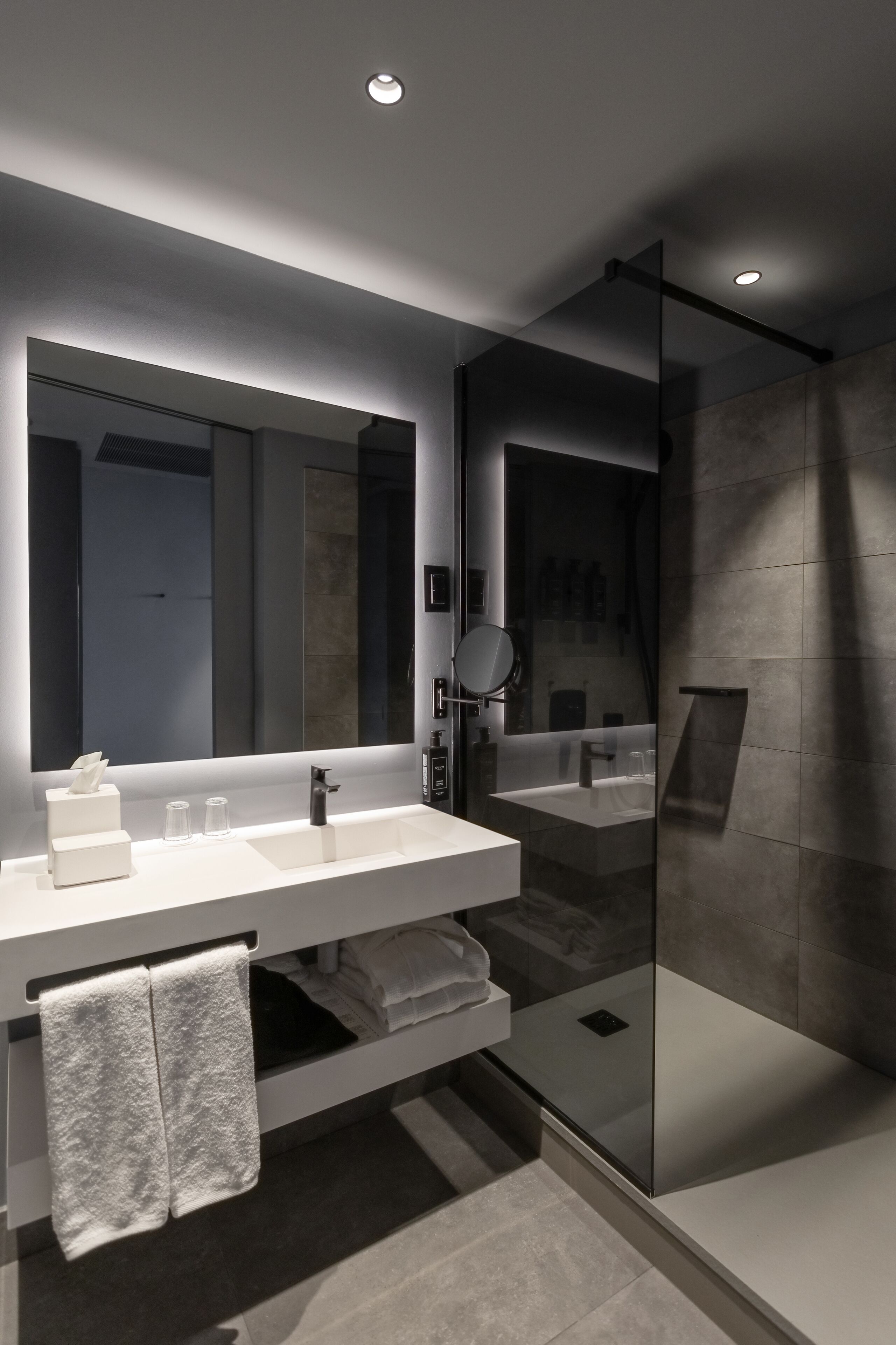 A modern bathroom with a large mirror, a white sink, and a glass-enclosed shower.
