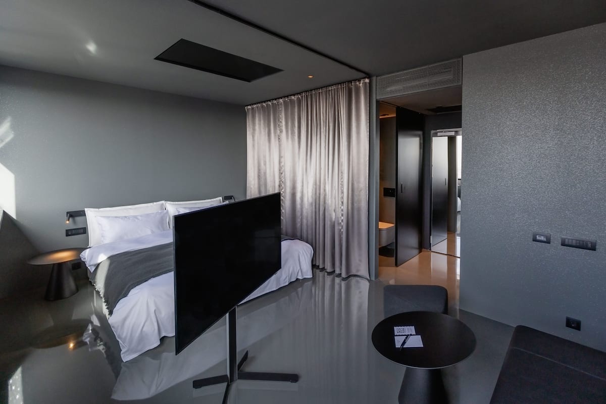 Habitación de hotel moderna con una cama grande, un televisor de pantalla plana, una pequeña mesa redonda y vistas al pasillo.