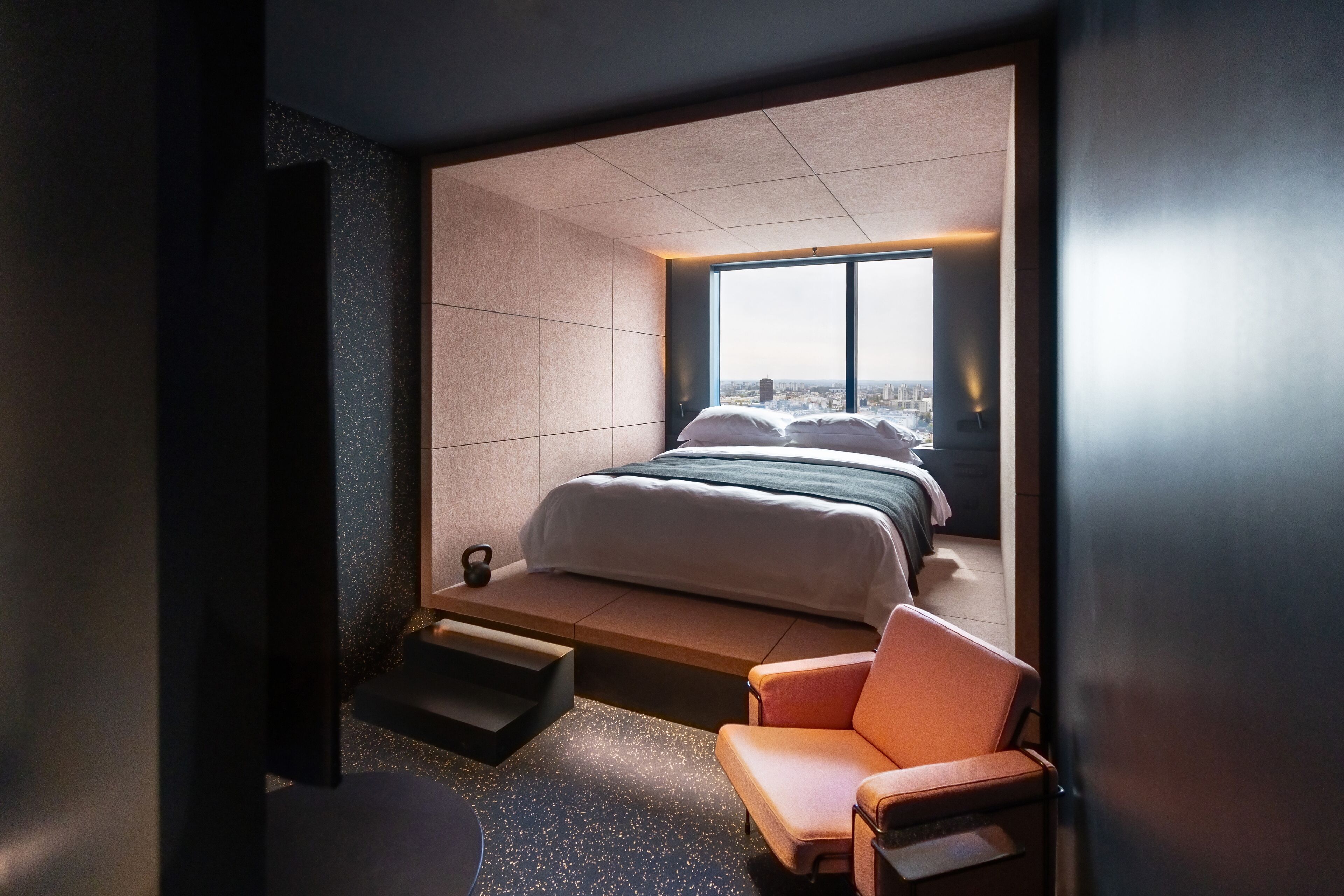 Una habitación de hotel moderna con una cama grande, una zona de estar y vistas a la ciudad a través de un amplio ventanal.