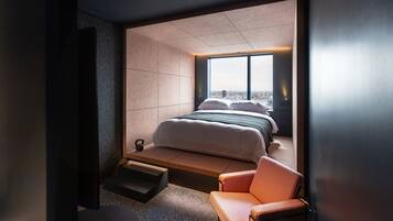 Una habitación de hotel moderna con una cama grande, una zona de estar y vistas a la ciudad a través de un amplio ventanal.