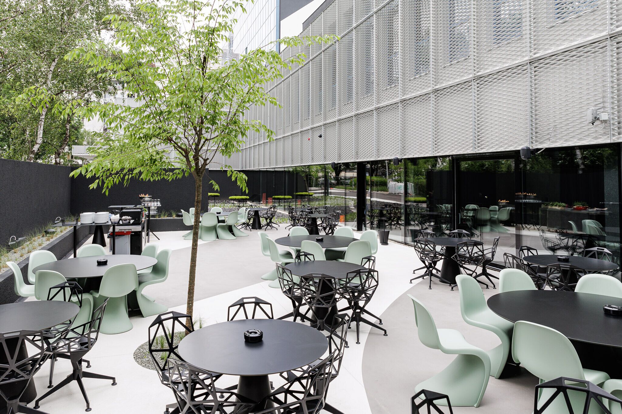 An outdoor café area with multiple tables and chairs, a grill, and a tree.