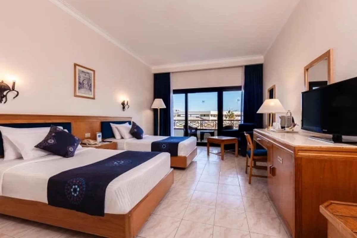 A hotel room with two beds, a desk, a television, and a view of the city.