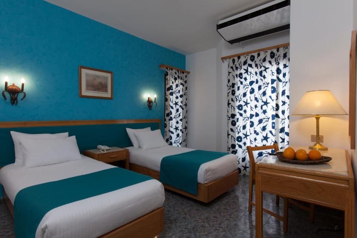 A hotel room with two beds, a desk with a lamp, and a picture on the wall.