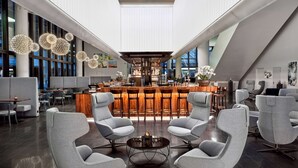 A modern hotel lobby with a bar area, seating arrangements, and large windows. - HYPERION Hotel Basel (Basel)