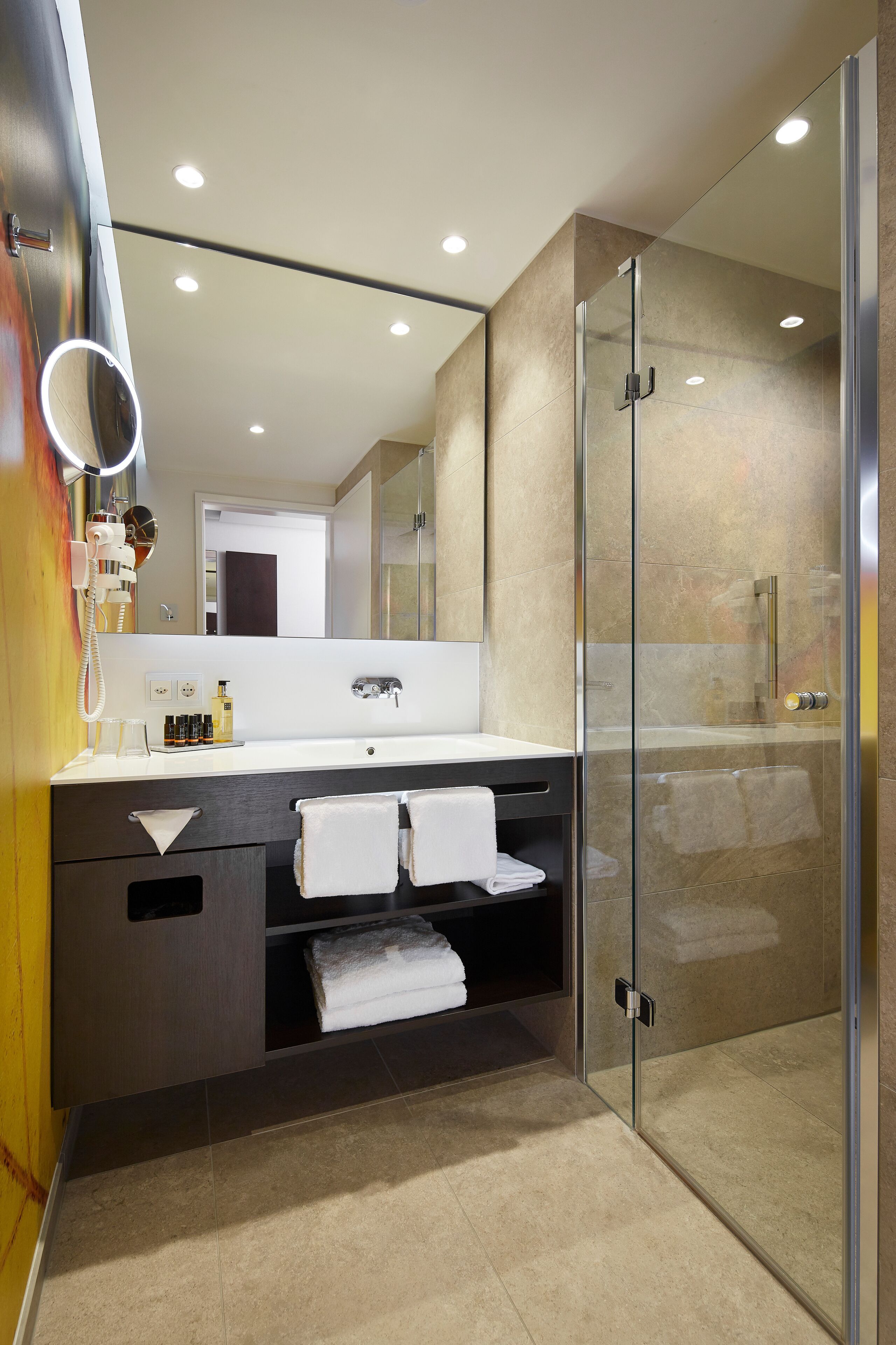 A modern bathroom with a glass-enclosed shower, a large mirror, and a vanity with a sink and towel rack.