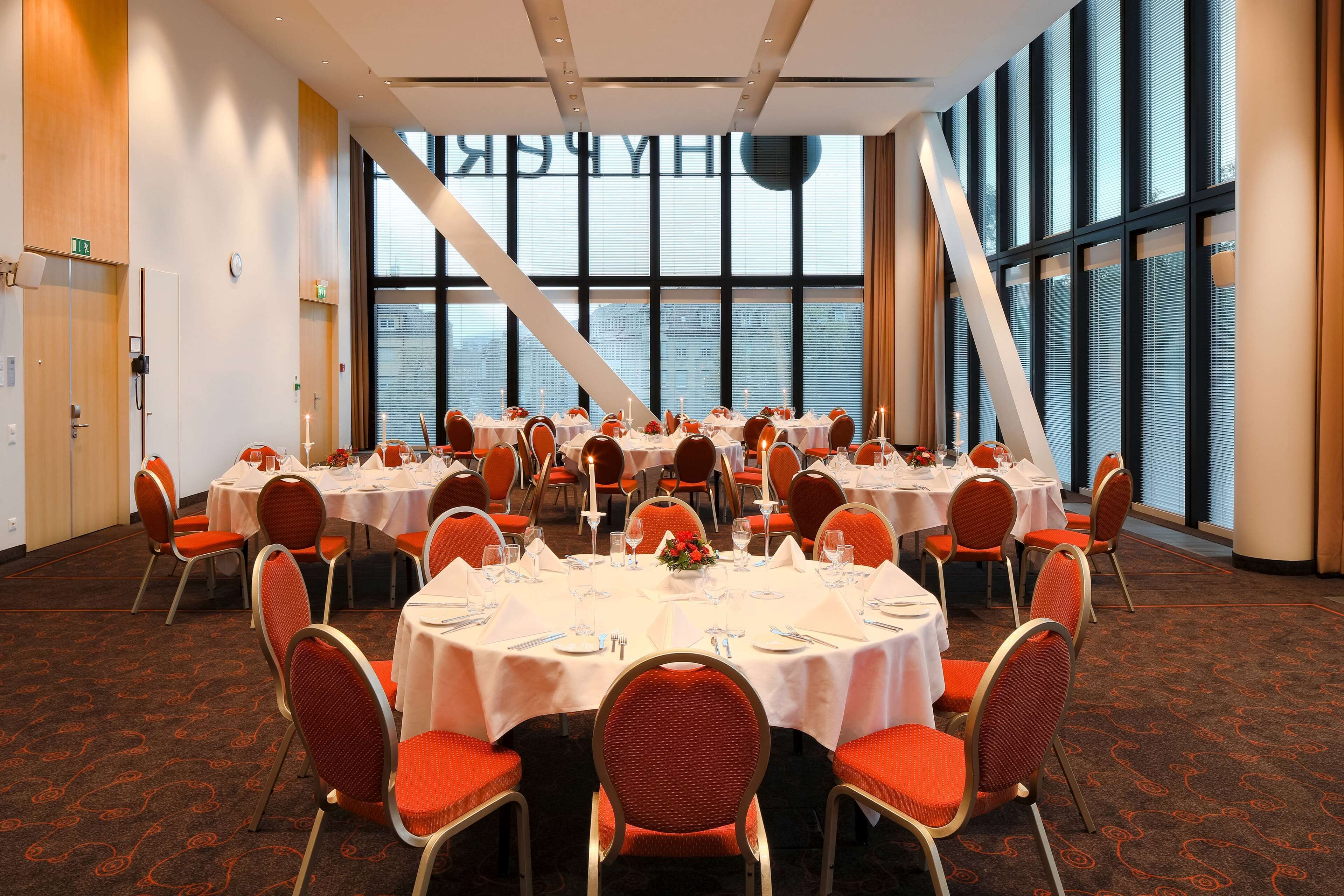 A conference room with round tables, orange chairs, and large windows offering a view of the city.