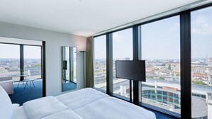 A hotel room with a large bed, a TV, and a view of the cityscape.