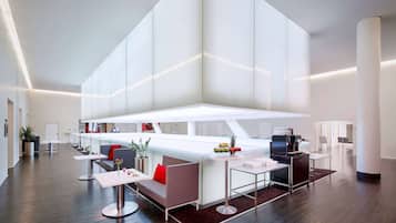 A modern hotel lobby with a central bar area, seating arrangements, and a high ceiling.