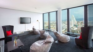 A modern hotel room with a large window, a flat-screen TV, and comfortable seating. - HYPERION Hotel Basel (Basel)