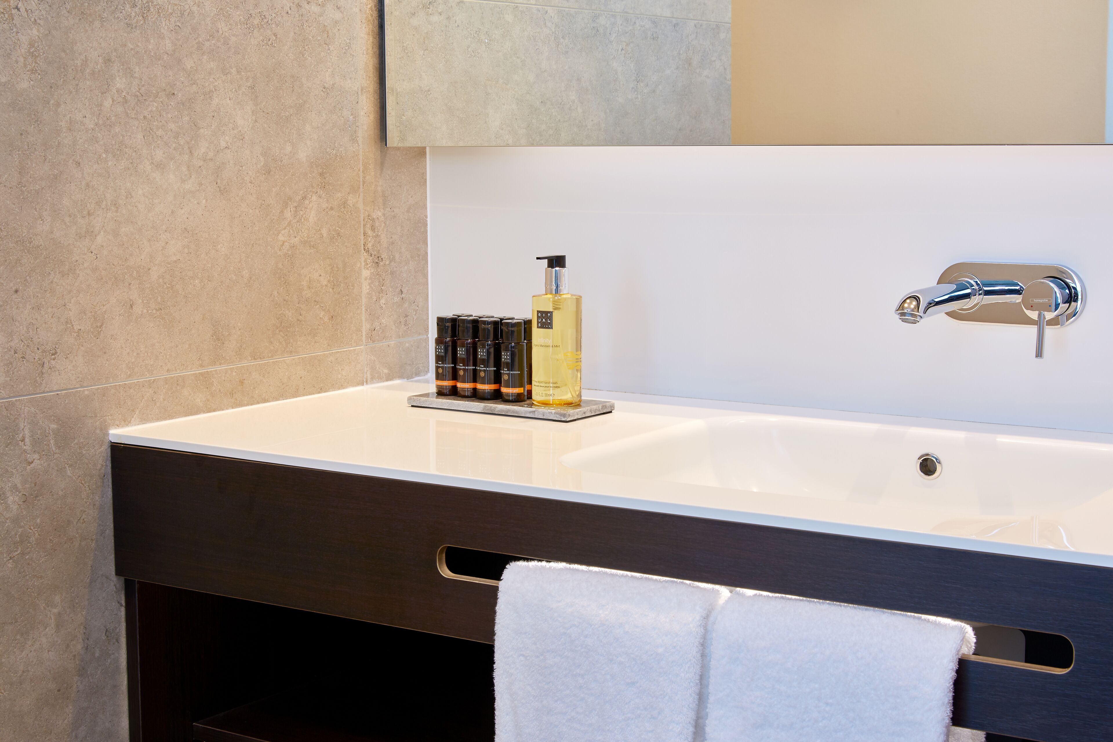 A modern bathroom with a large white sink, a dark vanity, a towel rack, and a bottle of shampoo.