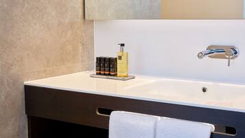 A modern bathroom with a large white sink, a dark vanity, a towel rack, and a bottle of shampoo.