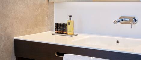 Un baño moderno con un lavamanos grande de color blanco, un mueble de tocador oscuro, un perchero y una botella de champú.