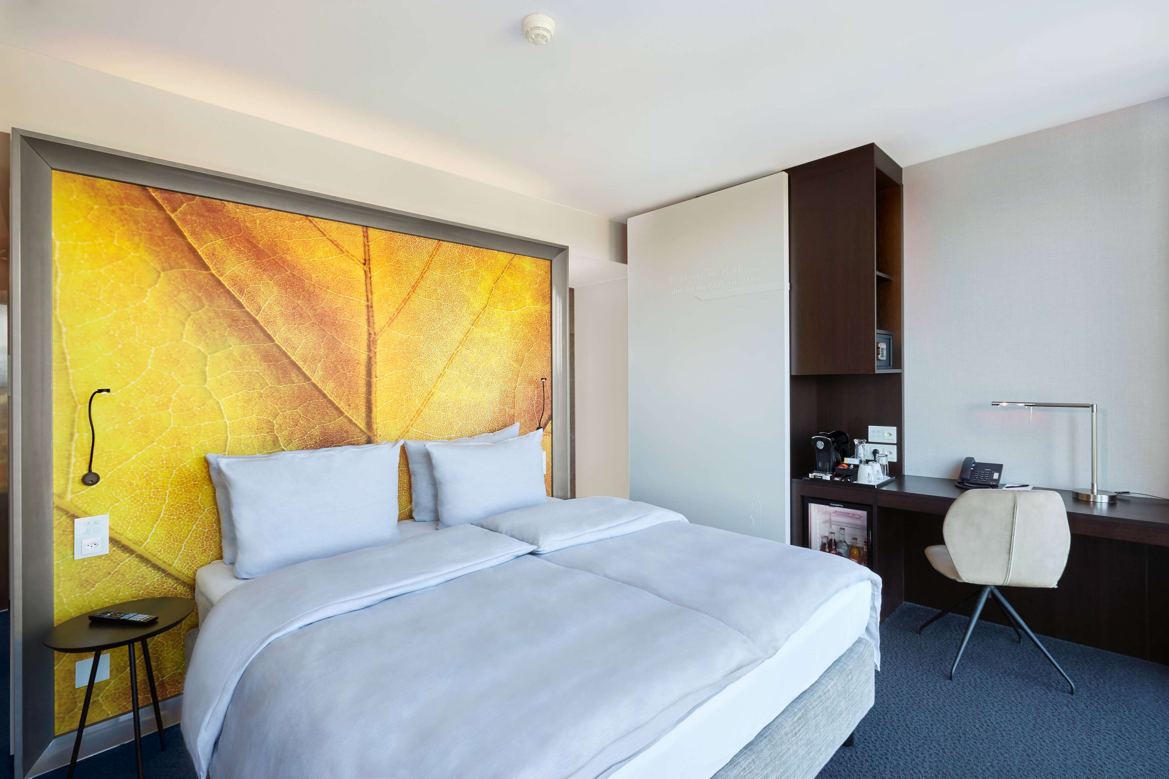 Habitación de hotel con una cama grande, un escritorio, una silla, una mesita y una pared con diseño texturizado.
