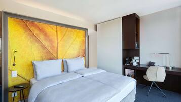 Habitación de hotel con una cama grande, un escritorio, una silla, una mesita y una pared con diseño texturizado.