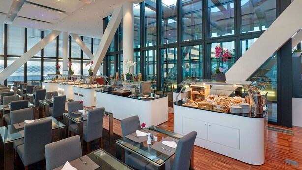 A modern dining area with glass tables, chairs, and a buffet station. - HYPERION Hotel Basel (Basel)