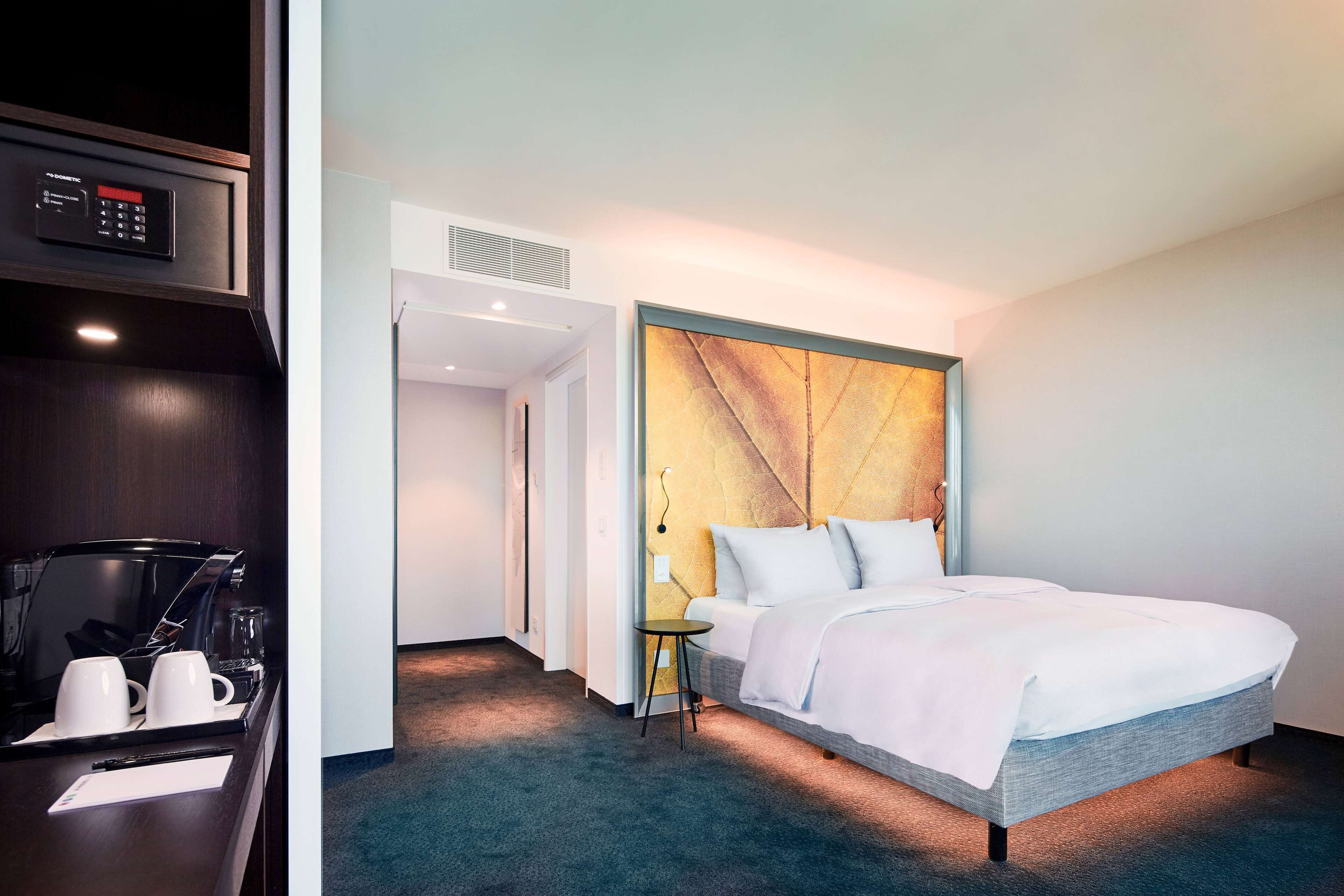 A hotel room with a bed, bedside table, and a control panel above the table.