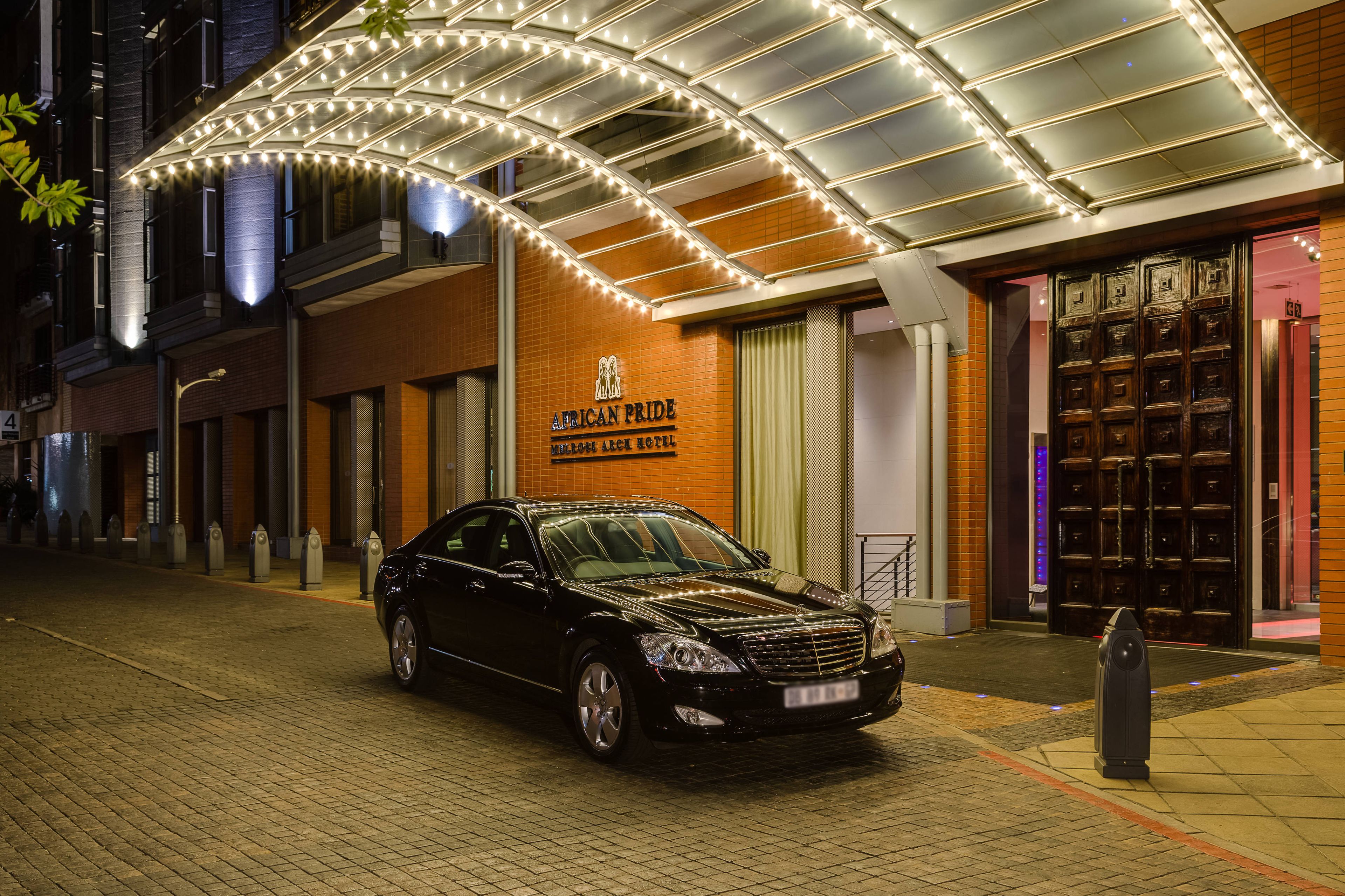 A black car parked in front of a hotel with a sign reading "African Pride."