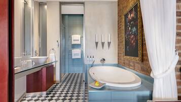 A modern bathroom with a large bathtub, a glass vanity, a black and white checkered floor, and a brick accent wall.