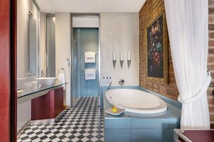 A modern bathroom with a large bathtub, a glass vanity, a black and white checkered floor, and a brick accent wall.