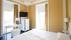 A hotel room with a large bed, a desk, a chair, a television, and a chandelier. - Greif Maria Theresia Hotel (Trieste)