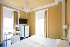 A hotel room with a large bed, a desk, a chair, a television, and a chandelier. - Greif Maria Theresia Hotel (Trieste)