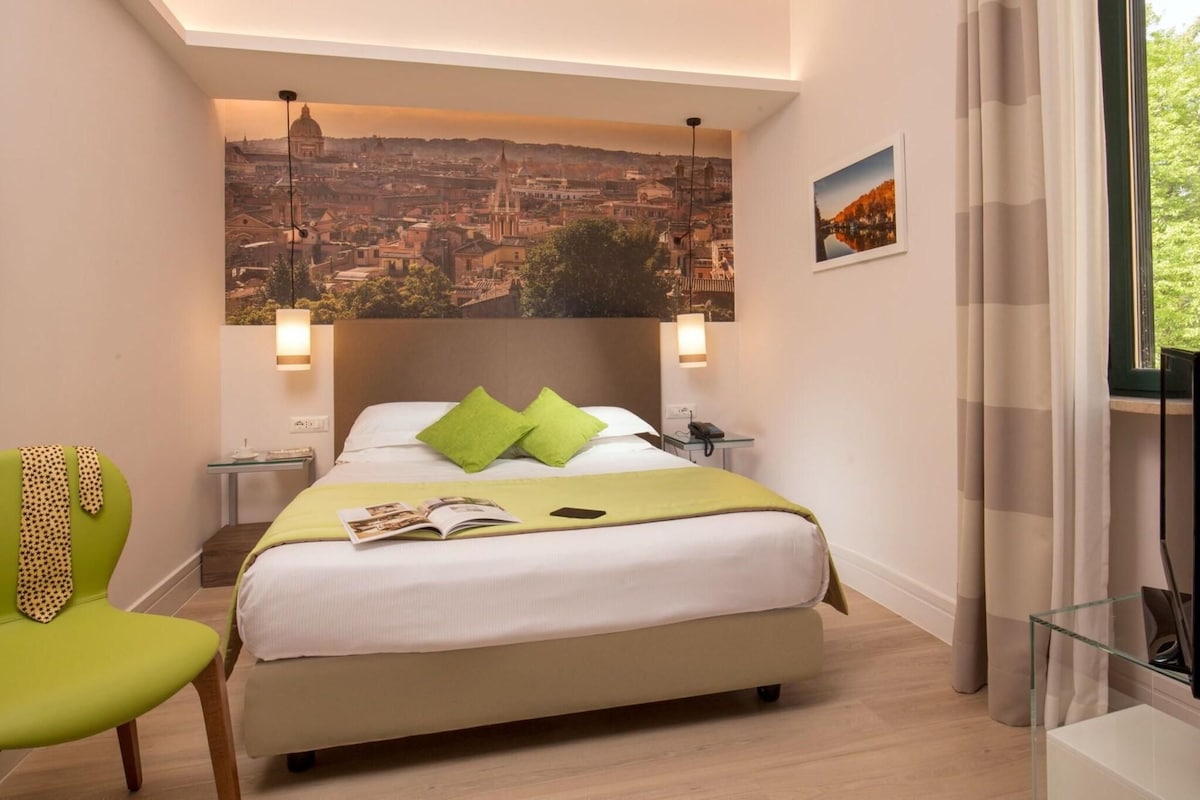 A hotel room with a bed, a chair, a nightstand, a lamp, a picture on the wall, and a window with curtains.