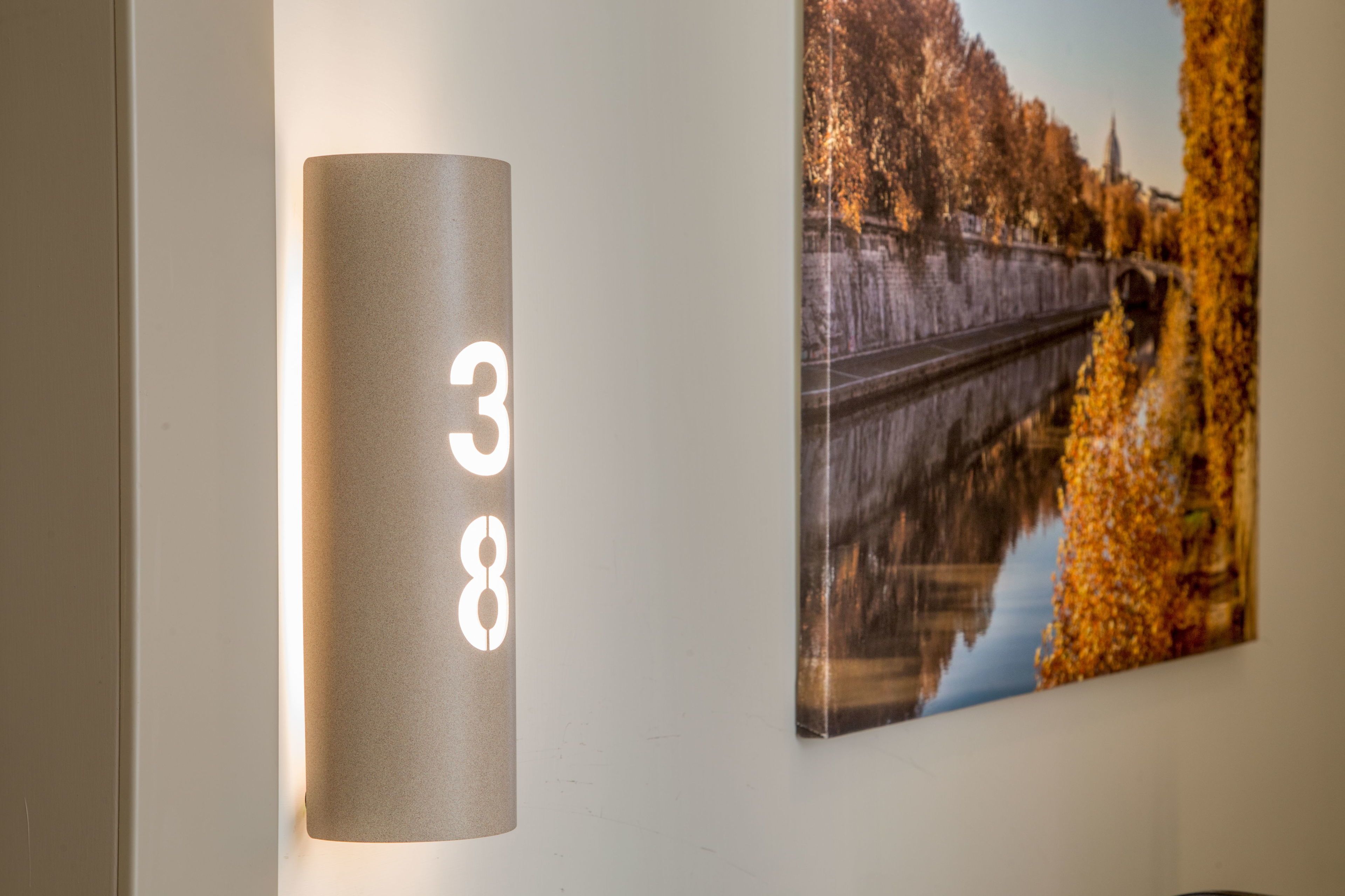 Een wandbevestigd nummerbord met de cijfers 38, een ingelijst foto van een brug met herfstbladeren en een lamp.