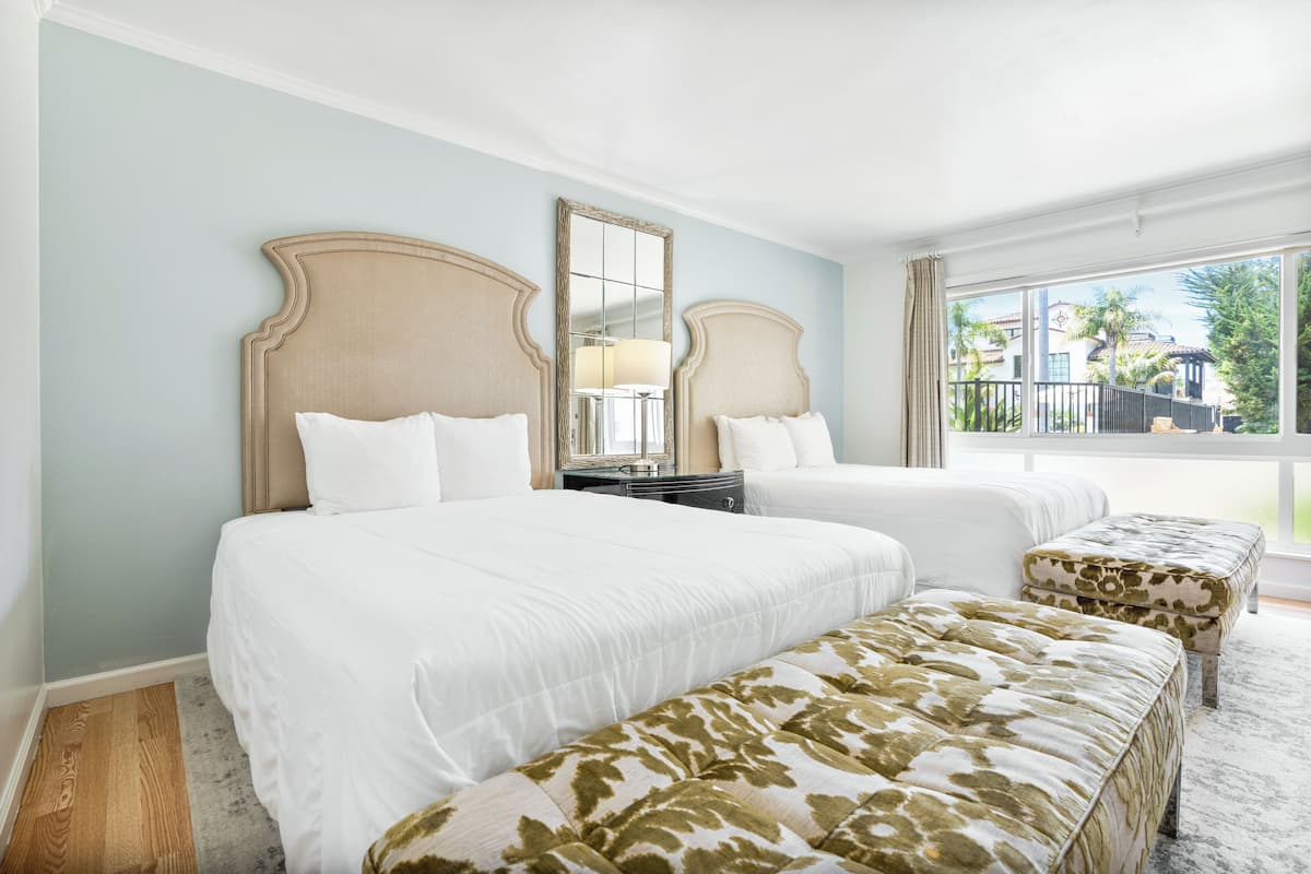 A hotel room with two beds, a large mirror, a nightstand, and a view of the outdoors.