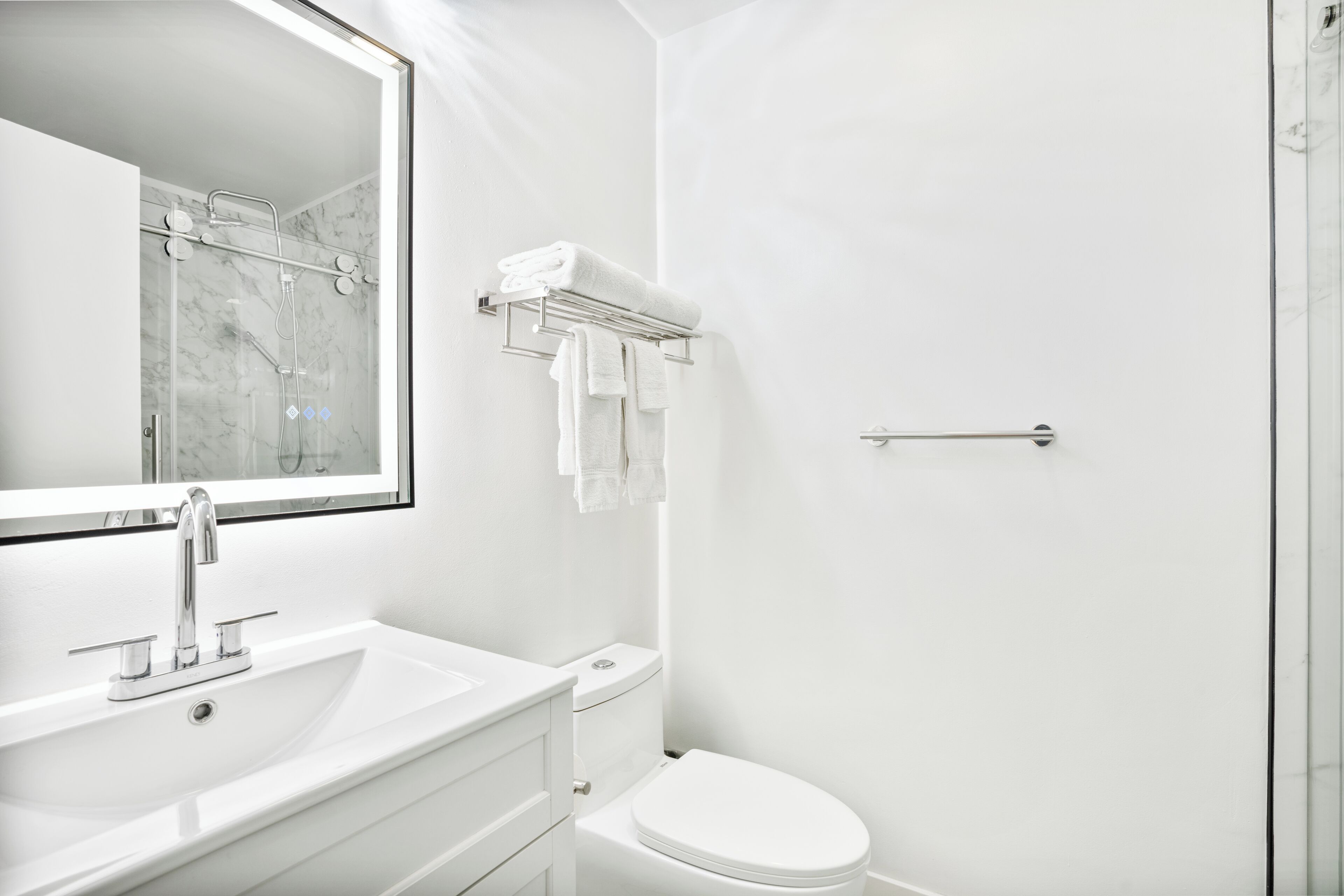 Een moderne badkamer met een wit wastafelmeubel, toilet en een douchecabine van glas.