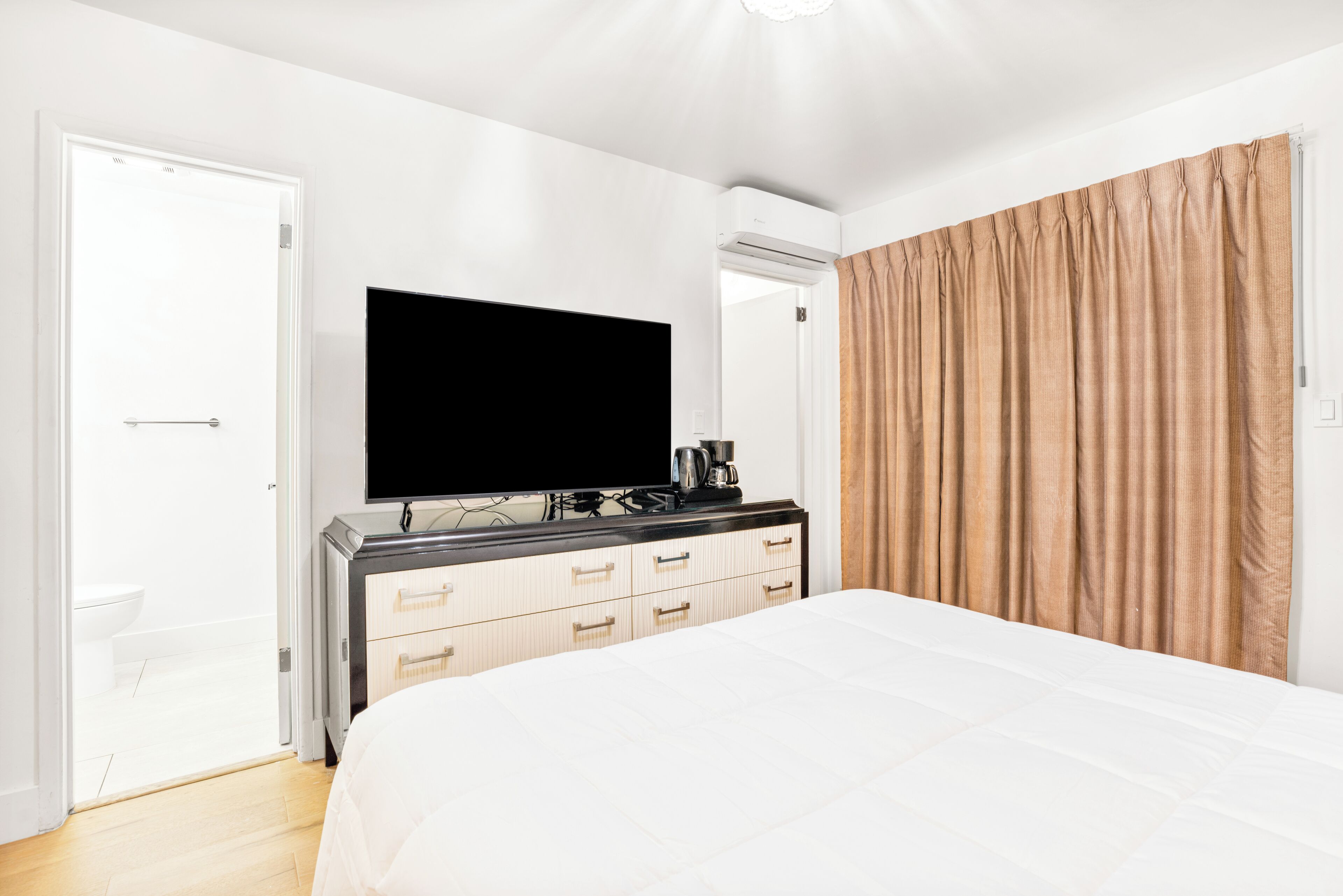 A hotel room with a bed, a television, a dresser, and a bathroom visible through an open door.